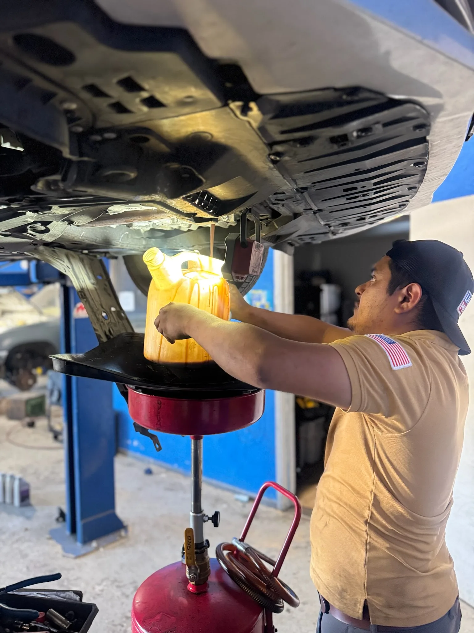 Technician draining engine oil from a car on a lift into an oil drain cart