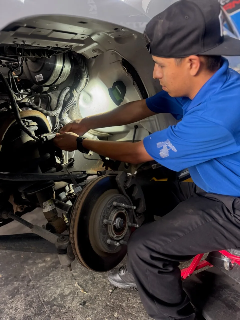 Technician crouched at a truck's front wheel hub and brake rotor with the wheel removed
