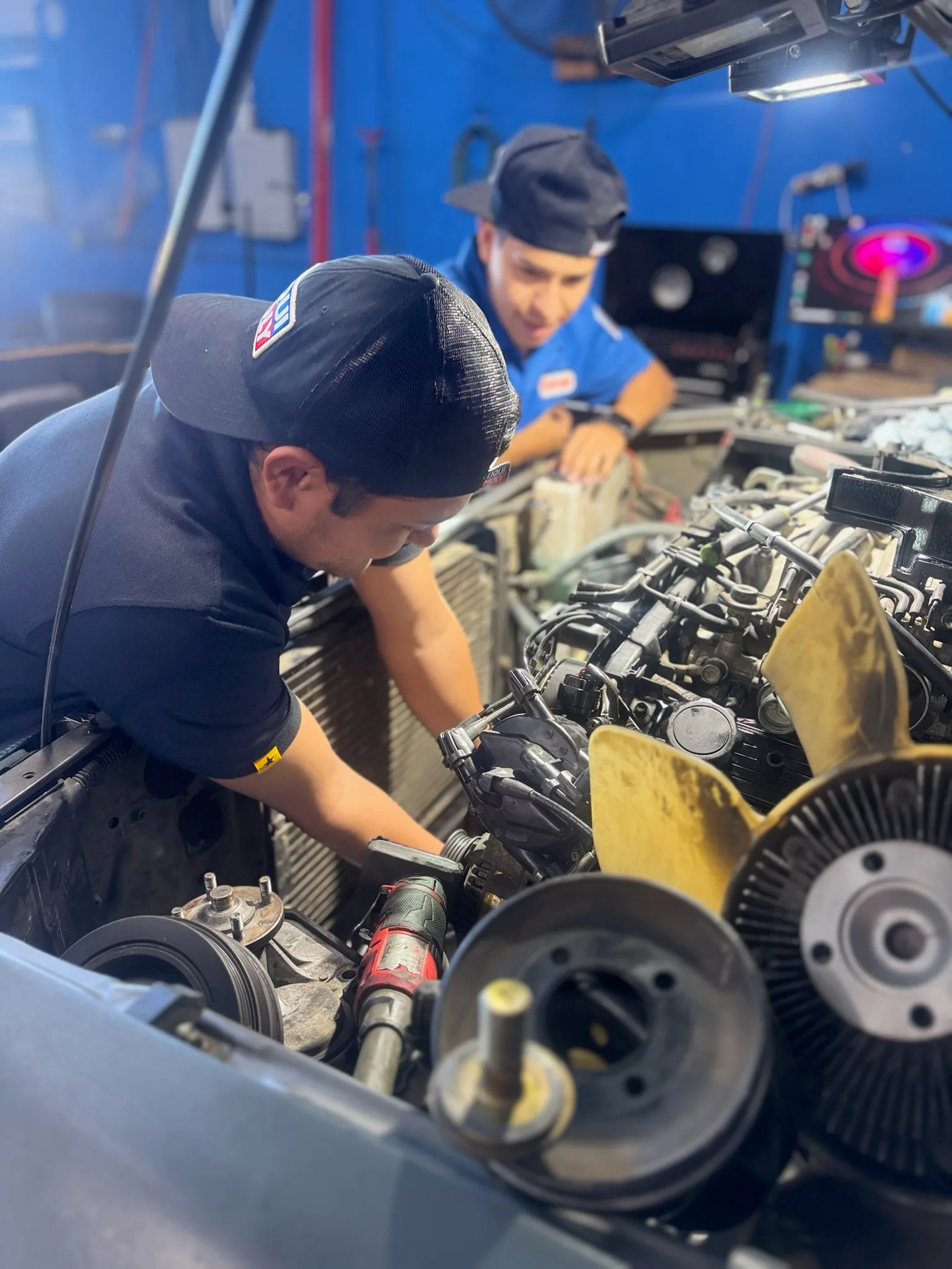 Two technicians working in an engine bay with the cooling fan and pulleys removed