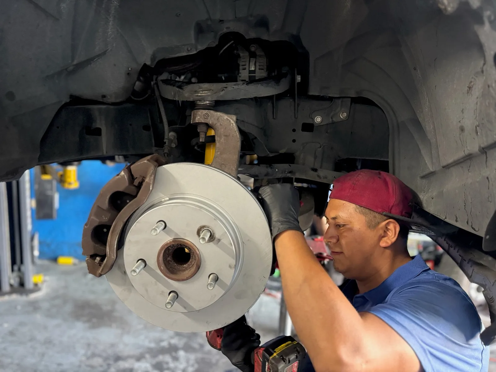 Technician installing a new brake rotor and caliper on a vehicle raised on a lift