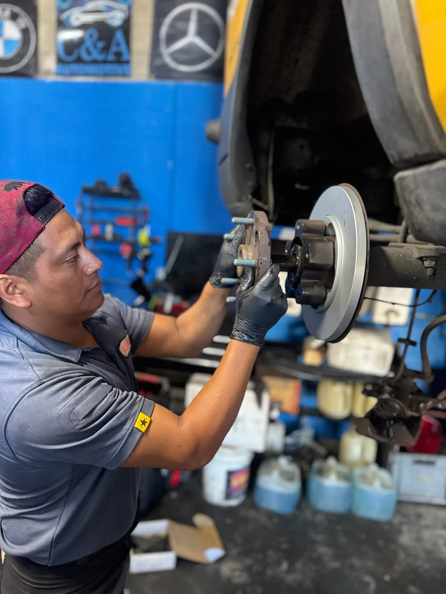 Technician in gloves fitting a brake rotor onto a wheel hub, with the C&A sign on the shop wall behind